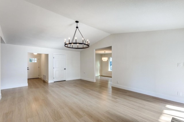 spare room featuring lofted ceiling, a healthy amount of sunlight, an inviting chandelier, and light hardwood / wood-style flooring