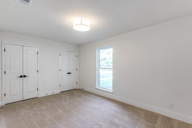 unfurnished bedroom featuring multiple closets and carpet flooring