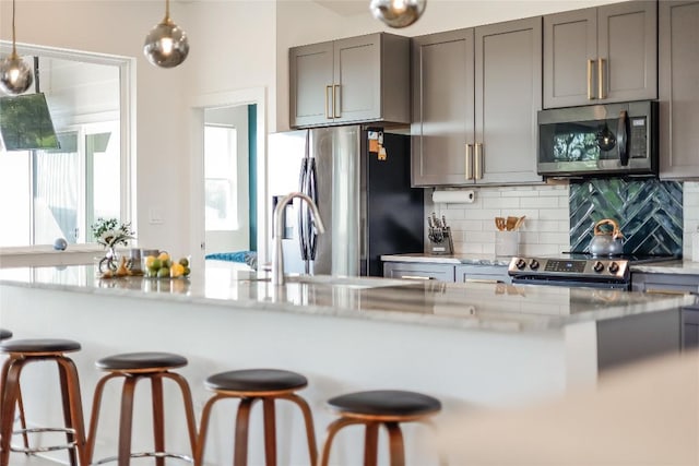 kitchen featuring hanging light fixtures, backsplash, light stone countertops, and appliances with stainless steel finishes