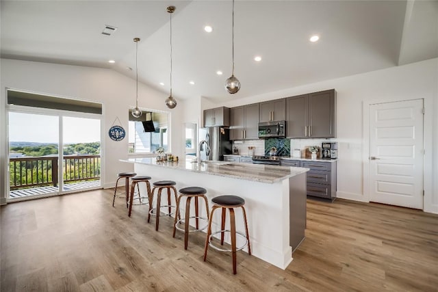 kitchen featuring stainless steel appliances, light stone counters, tasteful backsplash, an island with sink, and a kitchen bar