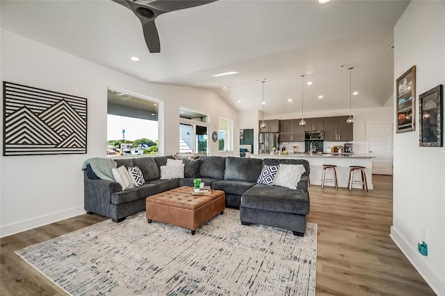 living room featuring vaulted ceiling, light wood-style flooring, ceiling fan, baseboards, and recessed lighting
