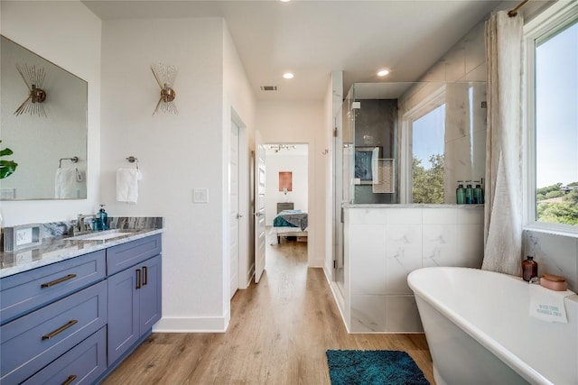 ensuite bathroom featuring wood finished floors, a stall shower, vanity, a freestanding tub, and recessed lighting