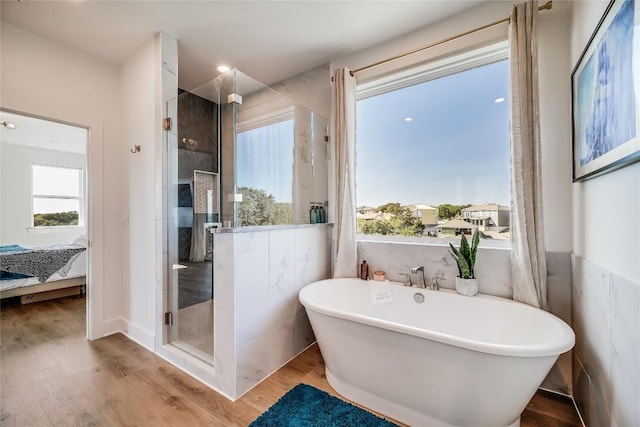 ensuite bathroom featuring plenty of natural light, a shower stall, a soaking tub, and wood finished floors