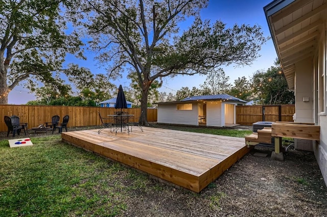 deck at dusk featuring an outdoor structure and a lawn