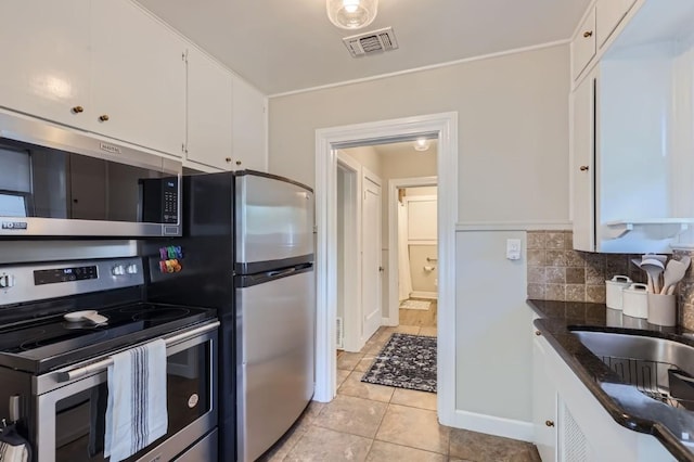 kitchen with white cabinetry, dark stone countertops, light tile patterned floors, stainless steel appliances, and decorative backsplash