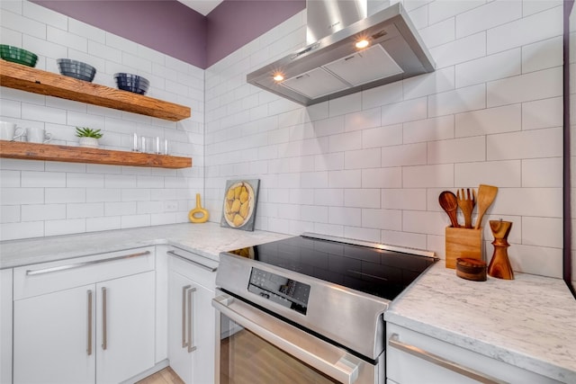 kitchen featuring stainless steel range with electric cooktop, wall chimney range hood, decorative backsplash, and white cabinetry