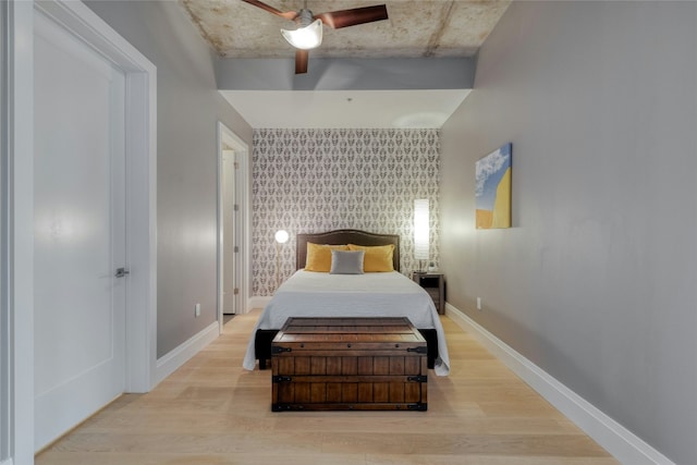 bedroom with an accent wall, ceiling fan, wood finished floors, baseboards, and wallpapered walls