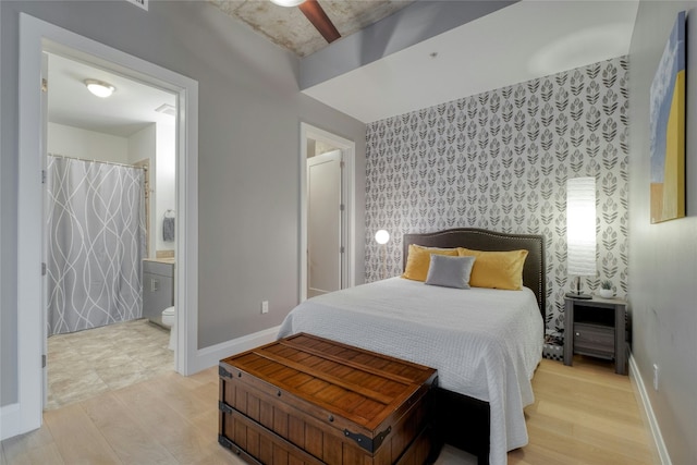 bedroom featuring connected bathroom, an accent wall, light wood-style floors, baseboards, and wallpapered walls