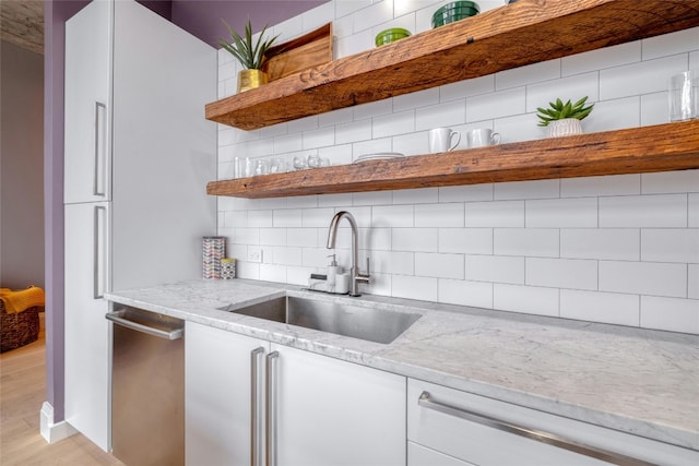 kitchen with light stone counters, a sink, dishwasher, open shelves, and tasteful backsplash