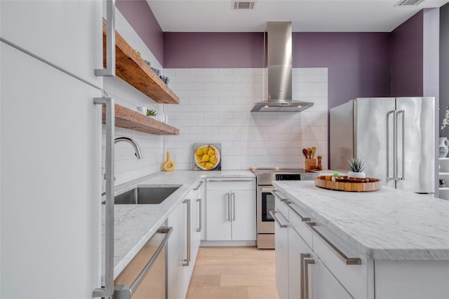 kitchen with stainless steel appliances, wall chimney range hood, white cabinetry, open shelves, and a sink