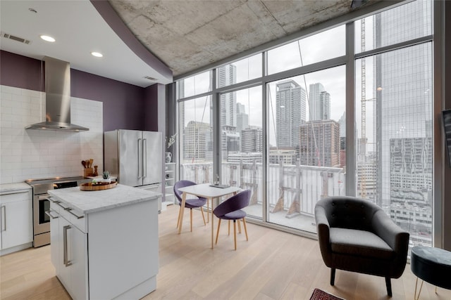 kitchen featuring a city view, floor to ceiling windows, visible vents, appliances with stainless steel finishes, and wall chimney range hood