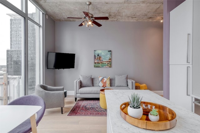 living area featuring ceiling fan, expansive windows, baseboards, and wood finished floors