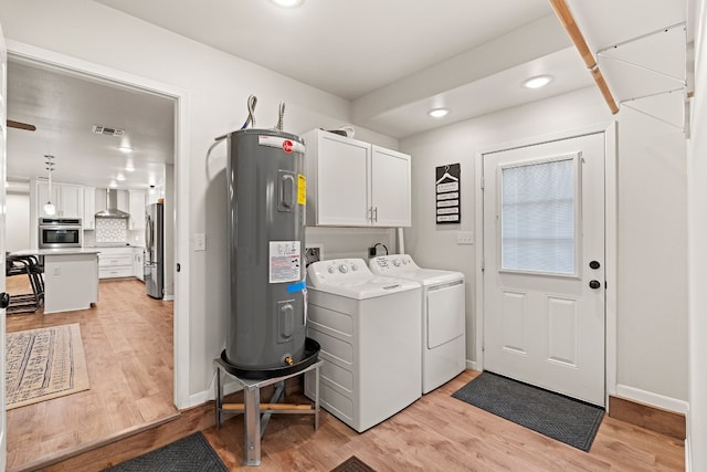 clothes washing area featuring cabinets, washing machine and dryer, water heater, and light hardwood / wood-style flooring