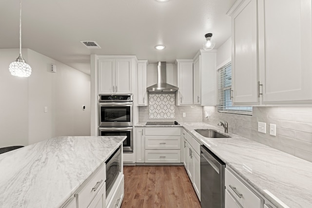 kitchen featuring appliances with stainless steel finishes, sink, white cabinets, hanging light fixtures, and wall chimney range hood