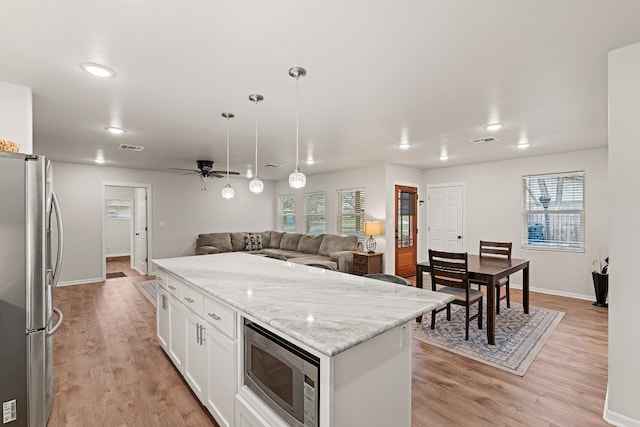 kitchen with pendant lighting, appliances with stainless steel finishes, a center island, light stone counters, and white cabinets