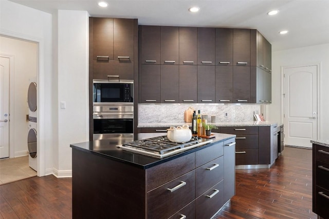 kitchen with dark hardwood / wood-style floors, a kitchen island, stacked washer and clothes dryer, and appliances with stainless steel finishes