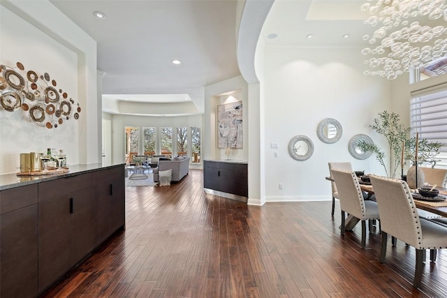 dining space featuring a raised ceiling, a healthy amount of sunlight, an inviting chandelier, and dark hardwood / wood-style flooring