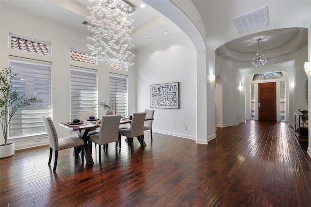 dining area featuring an inviting chandelier, a towering ceiling, dark hardwood / wood-style flooring, and a raised ceiling