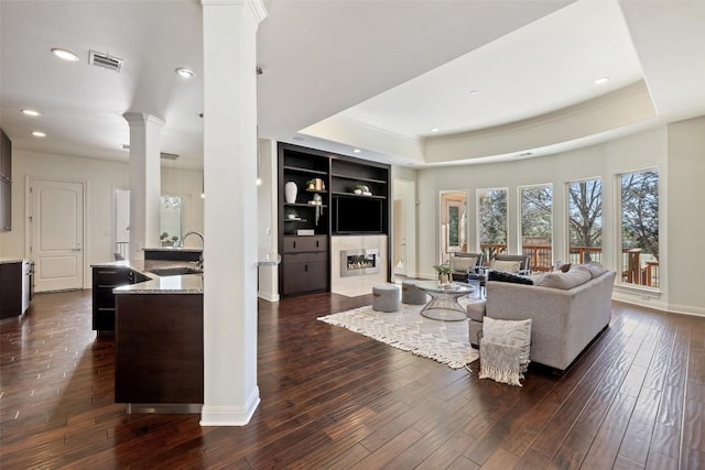 living room with decorative columns, sink, dark hardwood / wood-style floors, and a tray ceiling