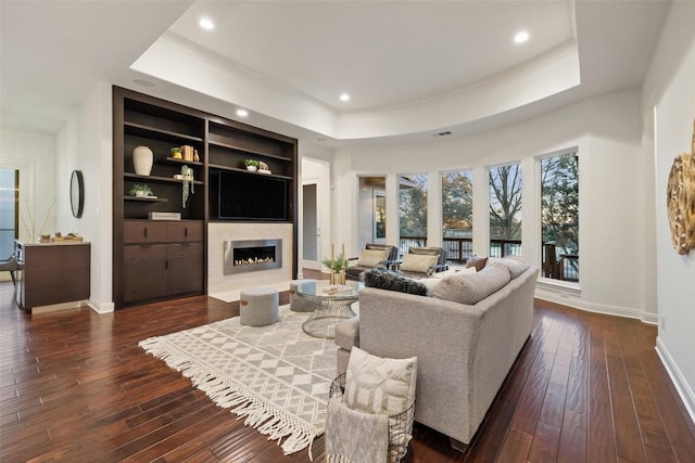 living room featuring dark hardwood / wood-style flooring, built in features, and a raised ceiling