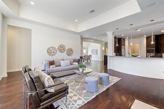 living room featuring dark hardwood / wood-style flooring, ornamental molding, a raised ceiling, and ornate columns