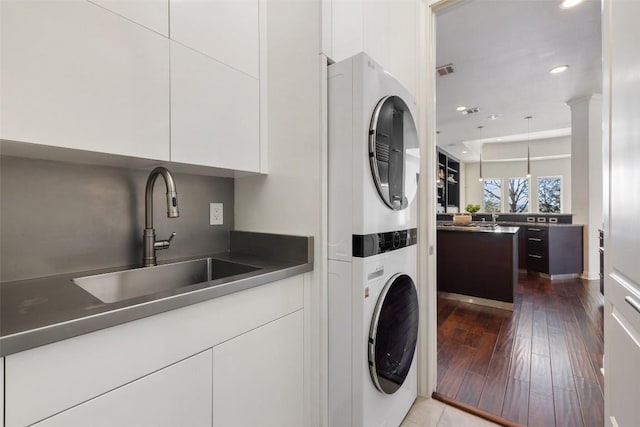 clothes washing area with sink, hardwood / wood-style flooring, cabinets, and stacked washer / dryer