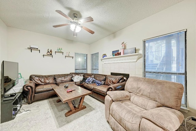 living room with a tiled fireplace, a textured ceiling, light colored carpet, and ceiling fan