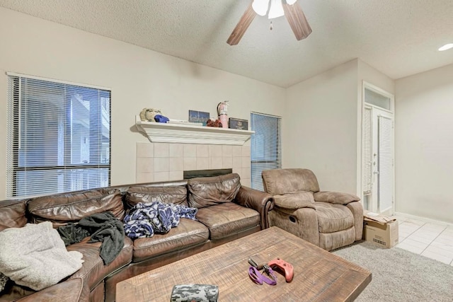 carpeted living room featuring a tiled fireplace, ceiling fan, and a textured ceiling