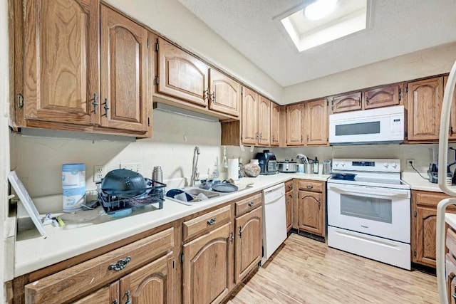 kitchen featuring sink, a skylight, a textured ceiling, light wood-type flooring, and white appliances