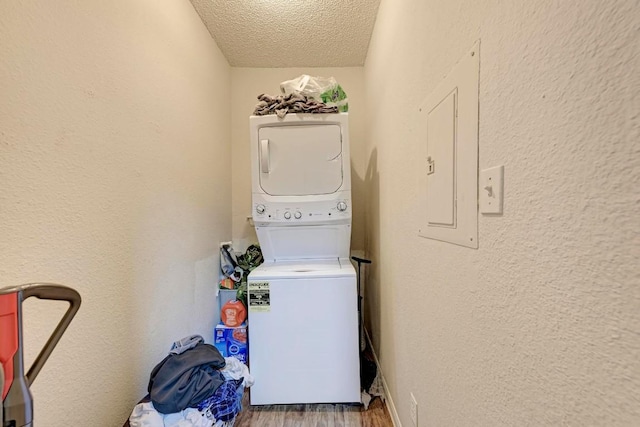 laundry area with stacked washer and dryer, wood-type flooring, electric panel, and a textured ceiling