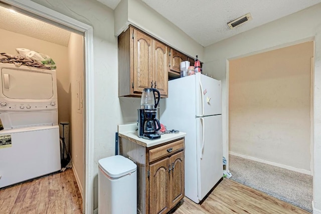 kitchen featuring light wood-type flooring, stacked washer and clothes dryer, a textured ceiling, and white fridge