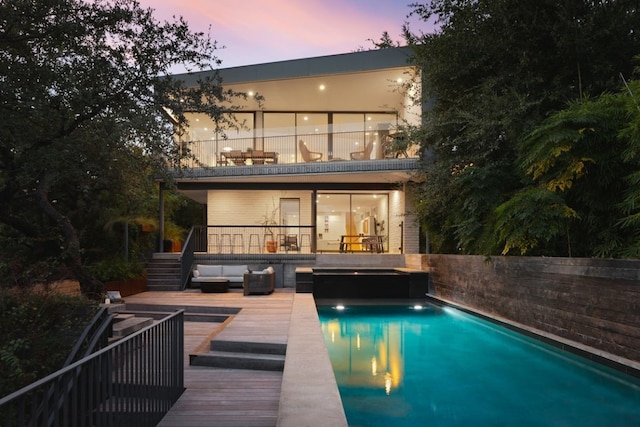 back house at dusk featuring a balcony, a swimming pool side deck, and outdoor lounge area