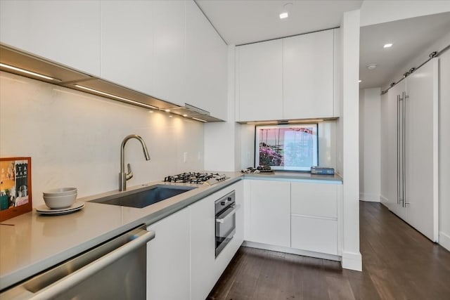 kitchen with sink, white cabinetry, stainless steel appliances, dark hardwood / wood-style floors, and a barn door