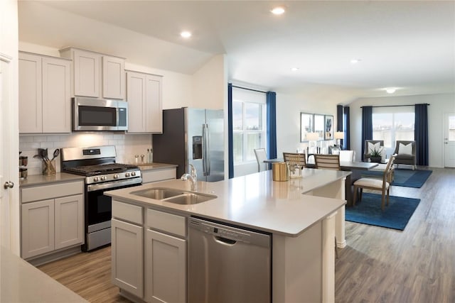 kitchen featuring sink, a center island with sink, stainless steel appliances, light hardwood / wood-style floors, and backsplash