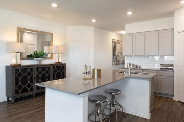 kitchen with gray cabinets, sink, dark hardwood / wood-style flooring, decorative backsplash, and a center island with sink