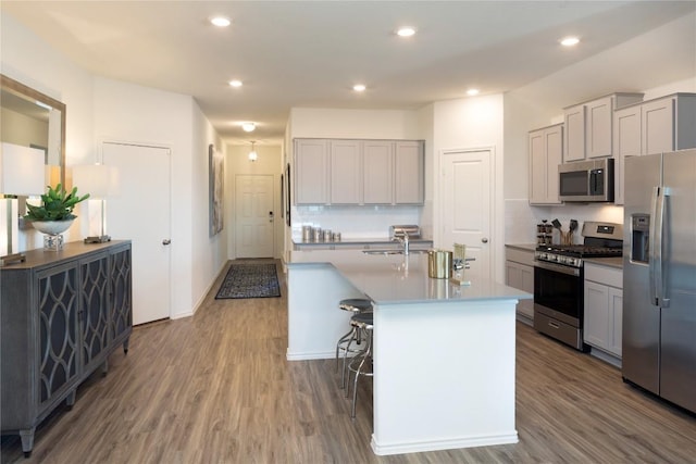 kitchen with appliances with stainless steel finishes, hardwood / wood-style floors, a center island with sink, and gray cabinetry