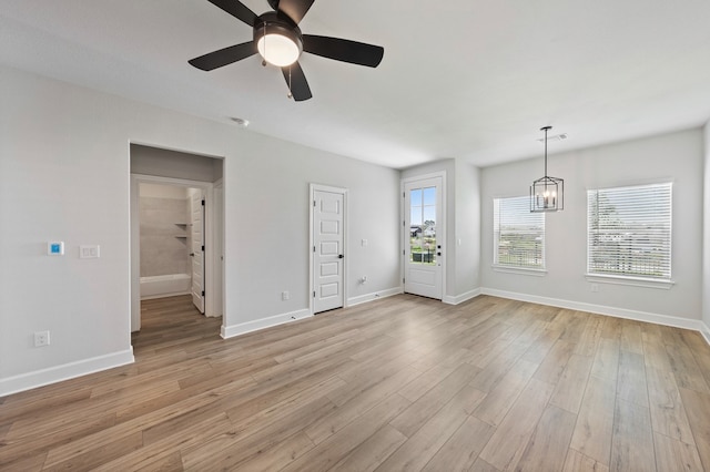 unfurnished living room featuring plenty of natural light, ceiling fan with notable chandelier, and light hardwood / wood-style flooring