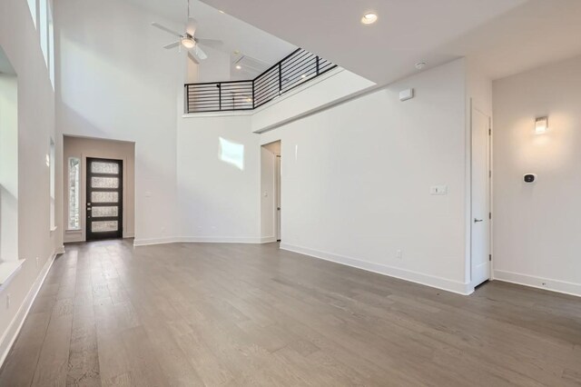 unfurnished living room with ceiling fan, dark hardwood / wood-style flooring, and a high ceiling