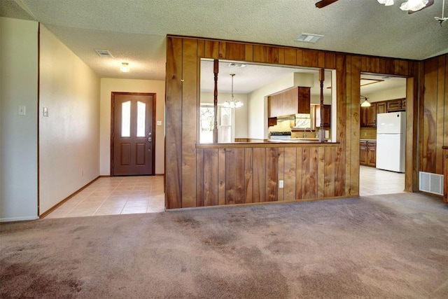 carpeted entrance foyer featuring ceiling fan with notable chandelier, wooden walls, and a textured ceiling