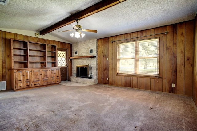 unfurnished living room featuring wooden walls, lofted ceiling with beams, light colored carpet, a brick fireplace, and a textured ceiling