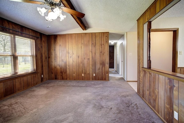 carpeted spare room with vaulted ceiling with beams, wooden walls, and a textured ceiling