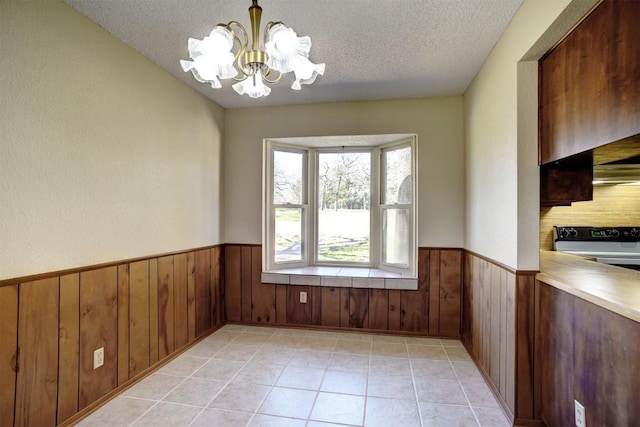 unfurnished dining area featuring an inviting chandelier, light tile patterned floors, a textured ceiling, and wood walls