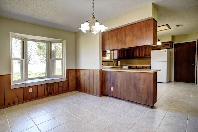 kitchen featuring decorative light fixtures, a chandelier, white refrigerator, kitchen peninsula, and a textured ceiling