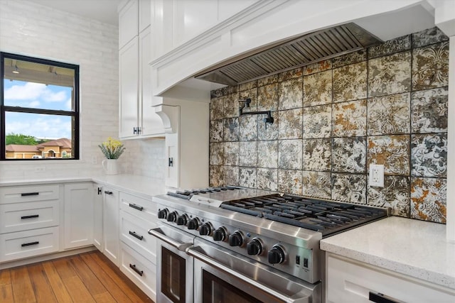 kitchen featuring white cabinetry, backsplash, range with two ovens, light stone counters, and custom range hood