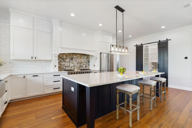 kitchen featuring pendant lighting, stainless steel refrigerator, white cabinetry, a center island, and a barn door