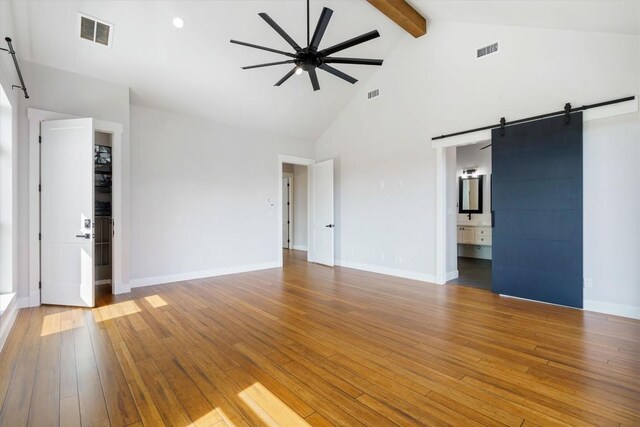 unfurnished living room featuring beam ceiling, high vaulted ceiling, hardwood / wood-style flooring, ceiling fan, and a barn door