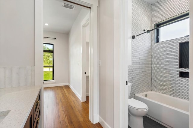 full bathroom with hardwood / wood-style flooring, tiled shower / bath, vanity, and toilet