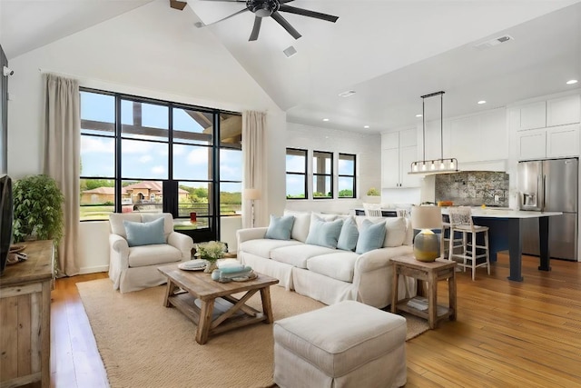 living room with high vaulted ceiling, ceiling fan, and light wood-type flooring