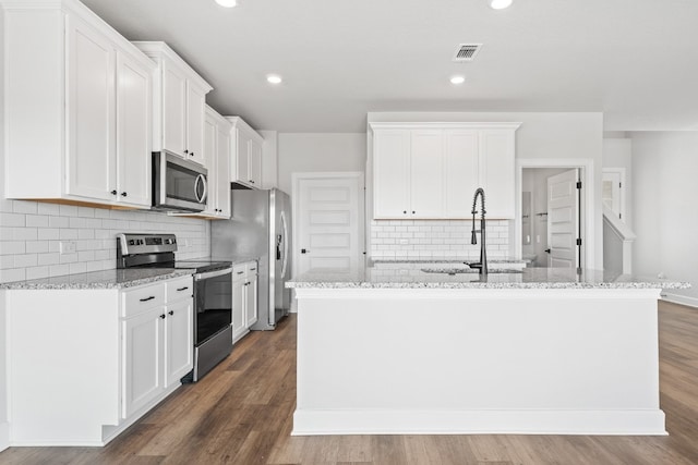 kitchen featuring appliances with stainless steel finishes, dark hardwood / wood-style flooring, light stone countertops, a kitchen island with sink, and white cabinets