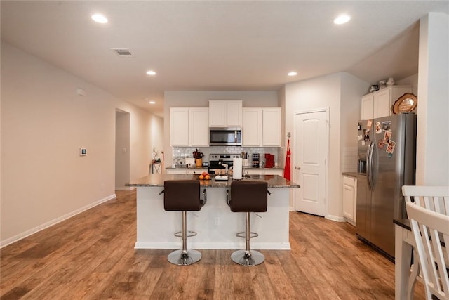 kitchen featuring a kitchen island with sink, white cabinetry, stainless steel appliances, and stone counters